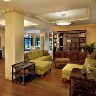 A modern living room with plush green sofas, a wooden bookshelf, and warm lighting.