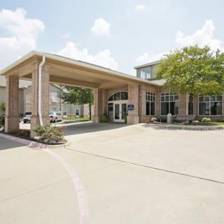 A building entrance with a covered driveway and surrounding trees on a sunny day.