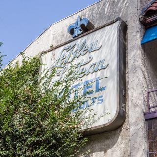 A vintage motel sign partially obscured by foliage on a sunny day.