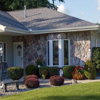 A well-maintained residential house with a stone facade, surrounded by neatly trimmed shrubs and a lush green lawn.