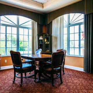 A cozy dining room with a round table, chairs, large windows, and elegant curtains.