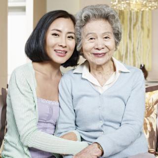 Two women, likely family members, smiling and sitting close together in a warmly lit room.