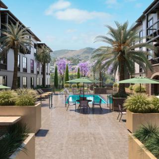 A scenic view of a resort complex featuring a swimming pool surrounded by palm trees and modern buildings.