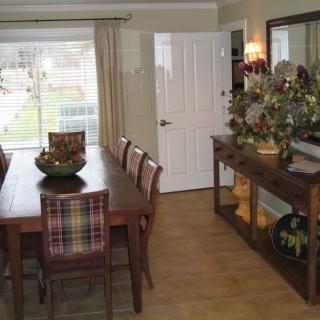 A cozy dining room with a wooden table and chairs, decorated with plants and a large mirror.