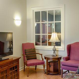 A cozy living room with a TV, comfortable chairs, and a warm lamp by the window.