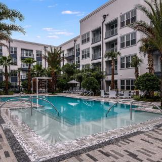 A luxurious apartment complex with a refreshing outdoor swimming pool surrounded by palm trees.