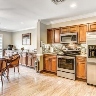 A modern kitchen with wood cabinets and stainless steel appliances, featuring an open dining area and hardwood floors.