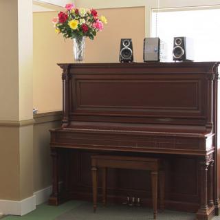 An upright piano with a vase of colorful flowers and speakers on top, placed in a cozy room.