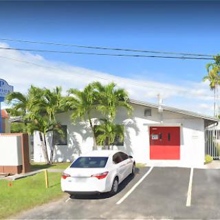 A bright and sunny day outside a small building with palm trees and a parked car.