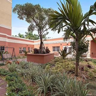 A serene courtyard garden with various plants and trees surrounded by red brick buildings.