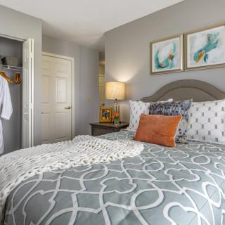 A cozy bedroom featuring an elegantly designed bed with patterned bedding, framed artwork, and a warm ambient lamp.