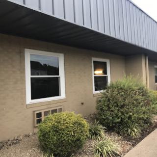 A view of the exterior of a commercial building featuring two windows and landscaped greenery.