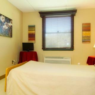 A cozy bedroom with a bed, artwork on the walls, and a window with blinds.