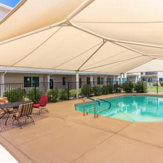A shaded outdoor swimming pool area with patio furniture.