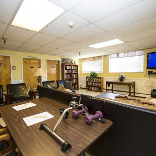 A multi-functional therapy room equipped with desks, chairs, exercise equipment, and a television.