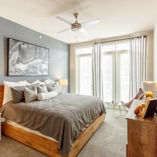 A modern and cozy bedroom with a large bed, soft lighting, and ample natural light from large windows.