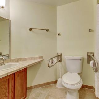 An accessible bathroom with a toilet equipped with handrails and a sink with a mirror above it.