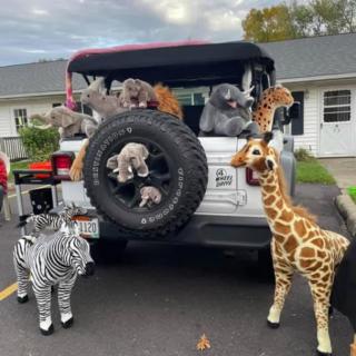 A parked Jeep decorated with various stuffed animals, including a giraffe, zebra, and koala.
