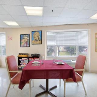 A cozy dining area with a table set for two, featuring posters on the walls and a large window providing natural light.
