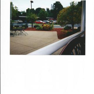 View of a parking lot from behind a railing, surrounded by greenery and flowers.