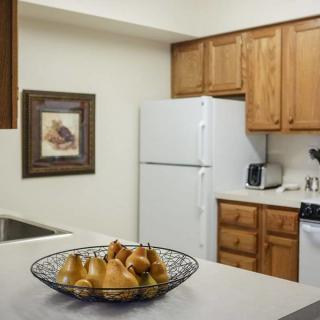 A cozy kitchen with wooden cabinets, a white refrigerator, and a fruit bowl filled with pears on the countertop.