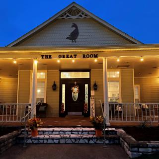 A warmly lit restaurant entrance with a welcoming front porch during nighttime.