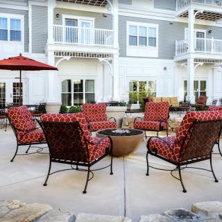 Outdoor seating area with red-cushioned chairs and a fire pit in front of a building.