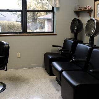 A salon interior with black chairs and hair dryers near a window.