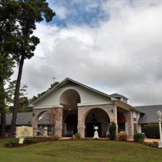 A picturesque building with a grand entrance, surrounded by a well-maintained lawn and tall trees under a cloudy sky.
