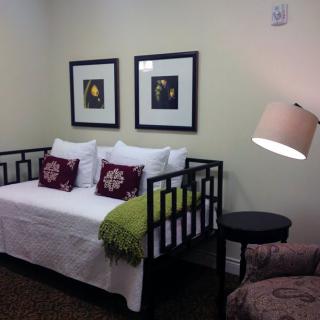 A cozy bedroom featuring a daybed, decorative pillows, framed artwork, and a standing lamp.