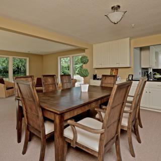 A spacious dining room featuring a large wooden table surrounded by chairs, with natural light streaming in through the windows.
