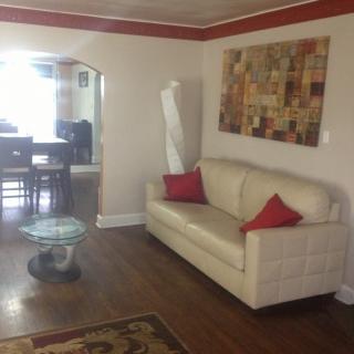 A cozy living room with a cream sofa, red accent pillows, and abstract wall art, leading into a dining area.