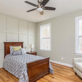 A cozy bedroom with a single bed, featuring wooden floors, modern decor, and large windows that allow natural light to fill the space.