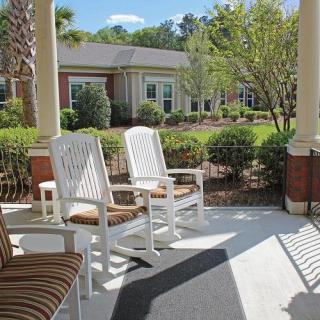 A peaceful porch with white rocking chairs overlooking a garden on a sunny day.