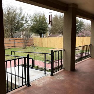 A porch with a ramp leading to a fenced garden area featuring trees and paved pathways.