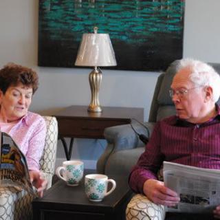 An elderly couple sits comfortably in their living room, enjoying reading and coffee together.
