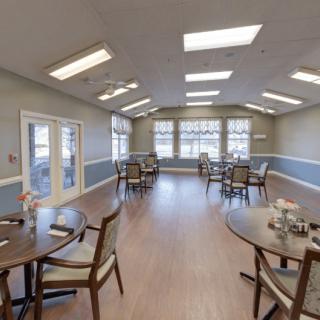 A spacious dining room with multiple tables and chairs, illuminated by skylights and large windows.