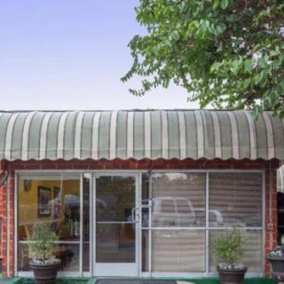 The entrance to a building features a green awning, glass doors, and potted plants on either side.