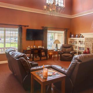 A cozy living room with leather sofas, a chandelier, and large windows providing natural light.