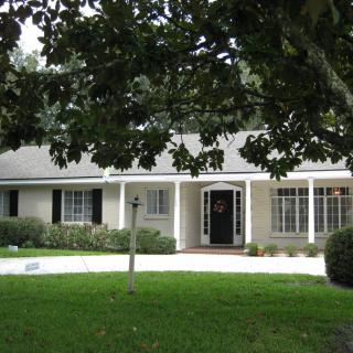 A quaint residential house with a front porch and a well-maintained lawn surrounded by trees.