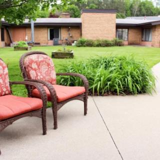Two cushioned chairs on a patio overlooking a lawn and building.