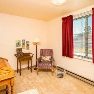 A cozy room with a chair, table, lamp, and a window with red curtains.