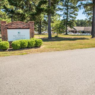 An inviting entrance featuring a sign surrounded by greenery and trees.