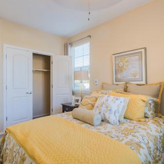 A cozy bedroom featuring a yellow and floral bedding set, with ample natural light and a closet.