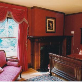 A cozy living room with antique furniture and a traditional fireplace, complemented by rich red curtains.