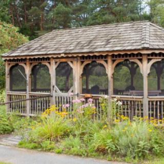 A wooden gazebo surrounded by lush garden greenery and flowers.