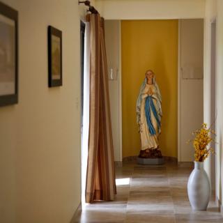 A hallway with a religious statue at the end, decorated with paintings and a vase.