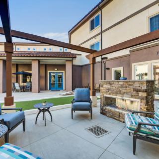 A modern outdoor patio with comfortable seating and a fireplace, set within a courtyard.