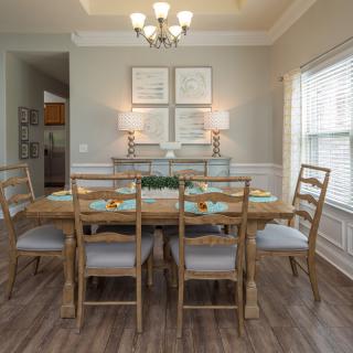 A neatly arranged dining room with a wooden table and chairs, highlighted by a chandelier and natural light from the windows.