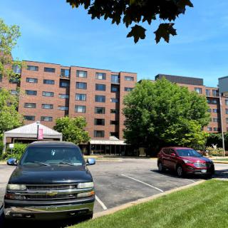A sunny day view of a residential building with parked cars and greenery.